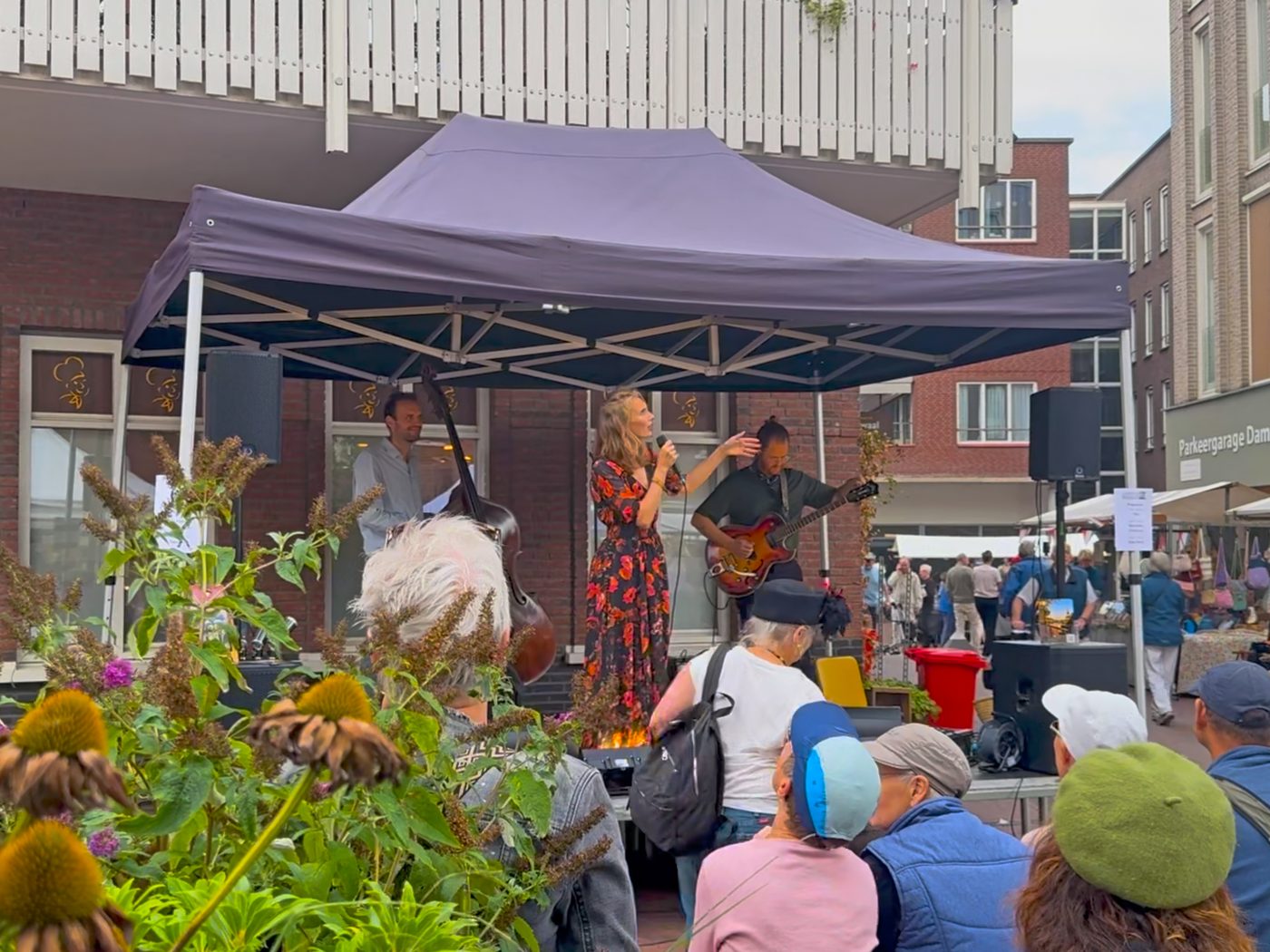 Publiek luistert tussen de bloemen naar een band op het podium